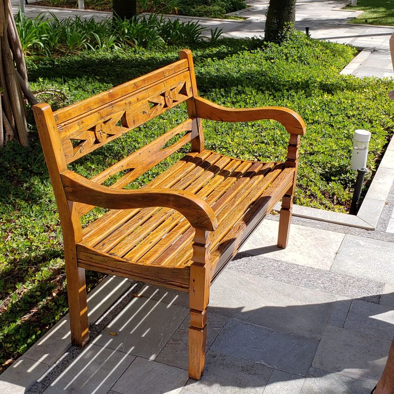 Banco de madeira maciça com braços e encosto vazado, em um jardim