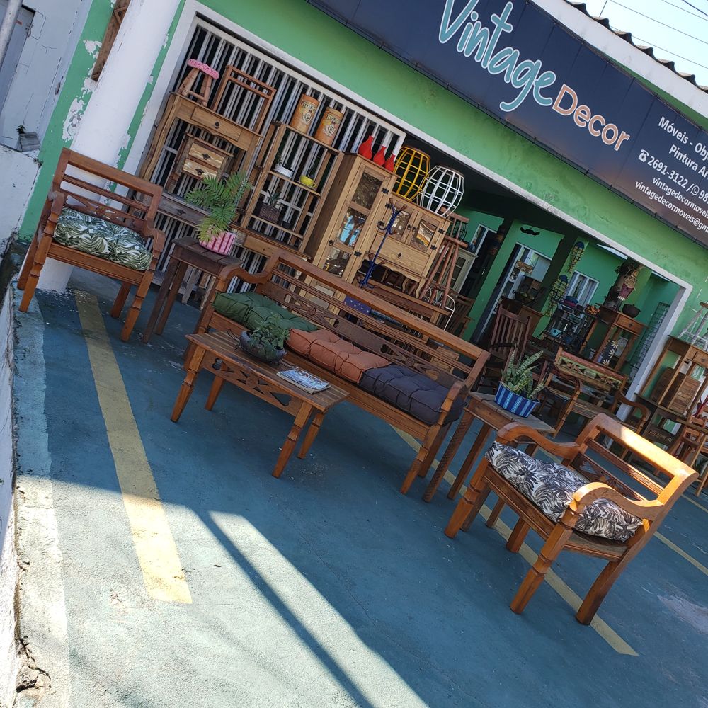Frente da loja vista de lado, com bancos e cadeiras de madeira expostos na calçada