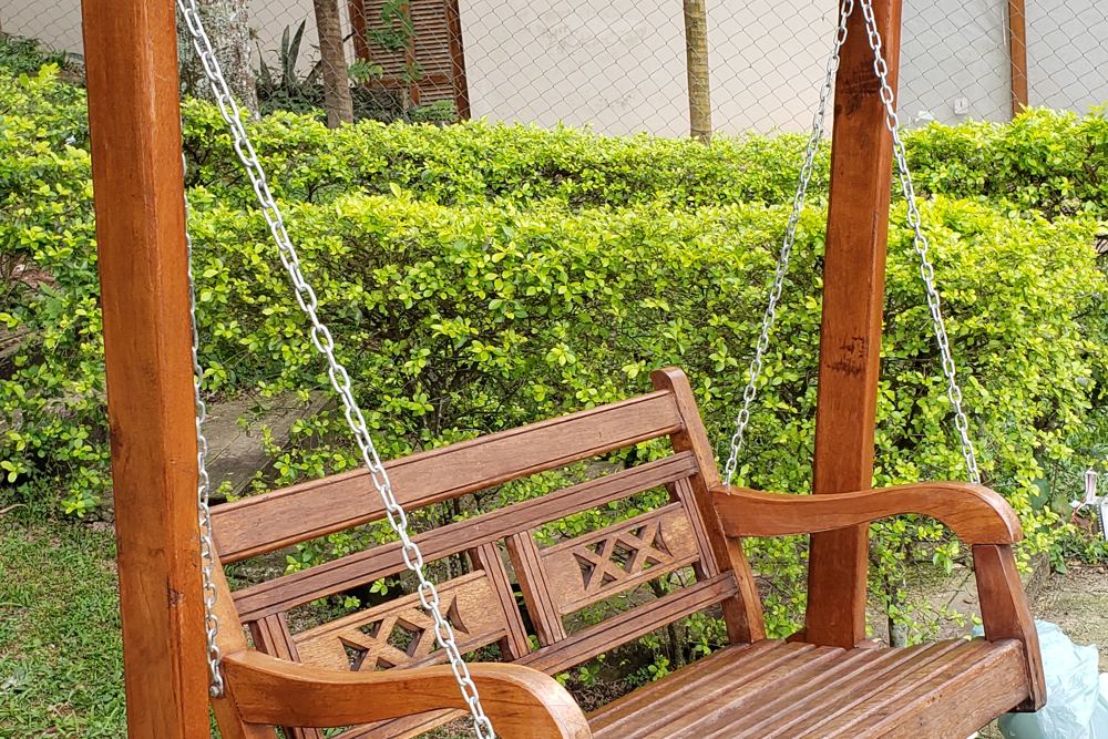 Balanço de madeira maciça pendurado por correntes na varanda de uma casa com jardim