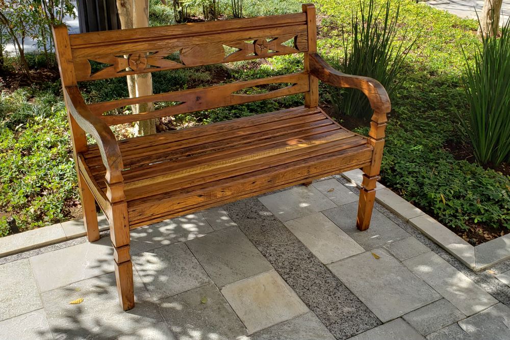 Banco de madeira maciça com encosto trabalhado, instalado em um jardim